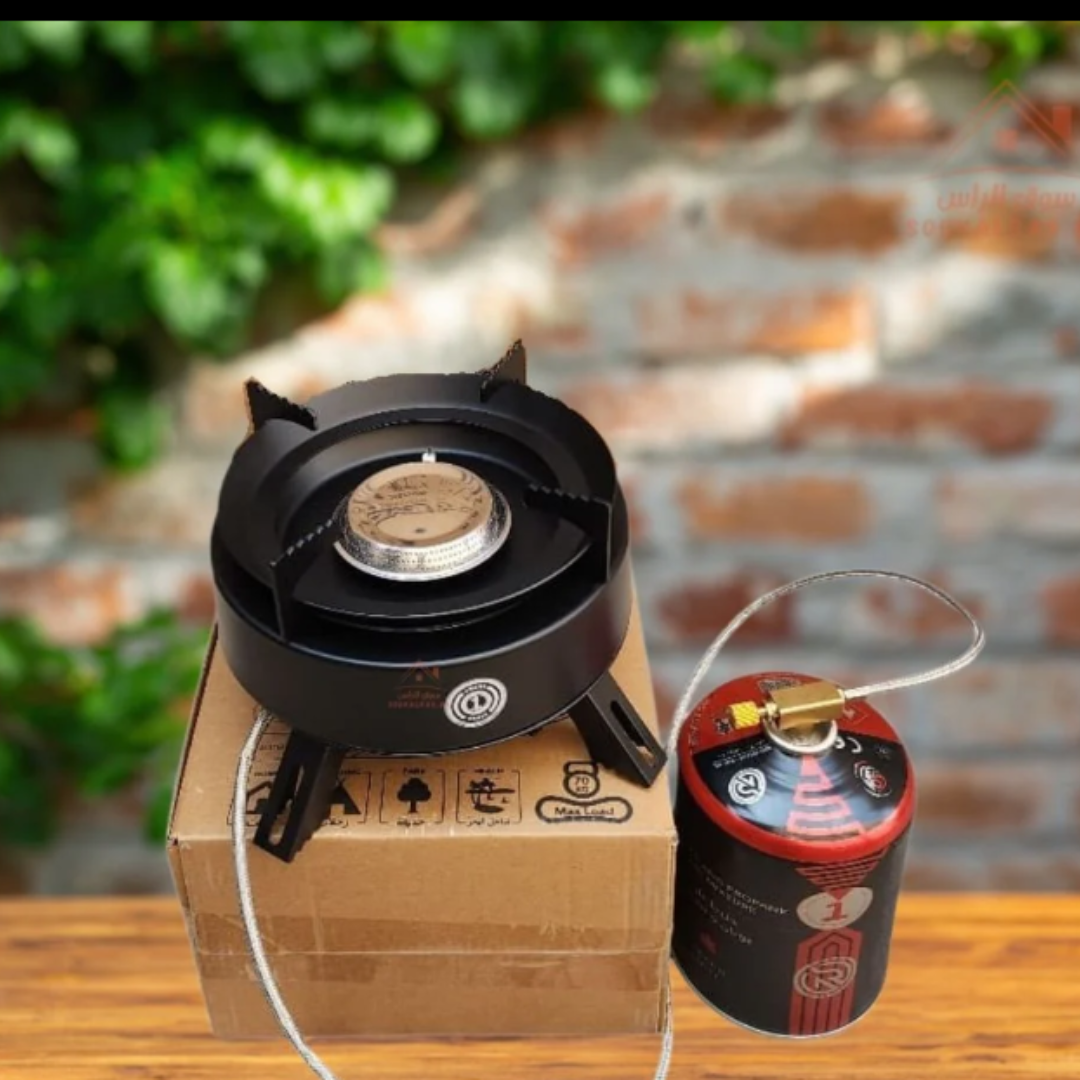 Portable gas stove on a cardboard box with a canister next to it, outdoors.